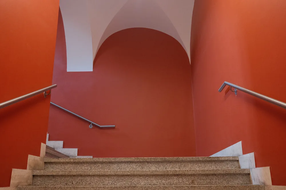 A stone staircase descending between red-orange walls beneath a white vaulted ceiling