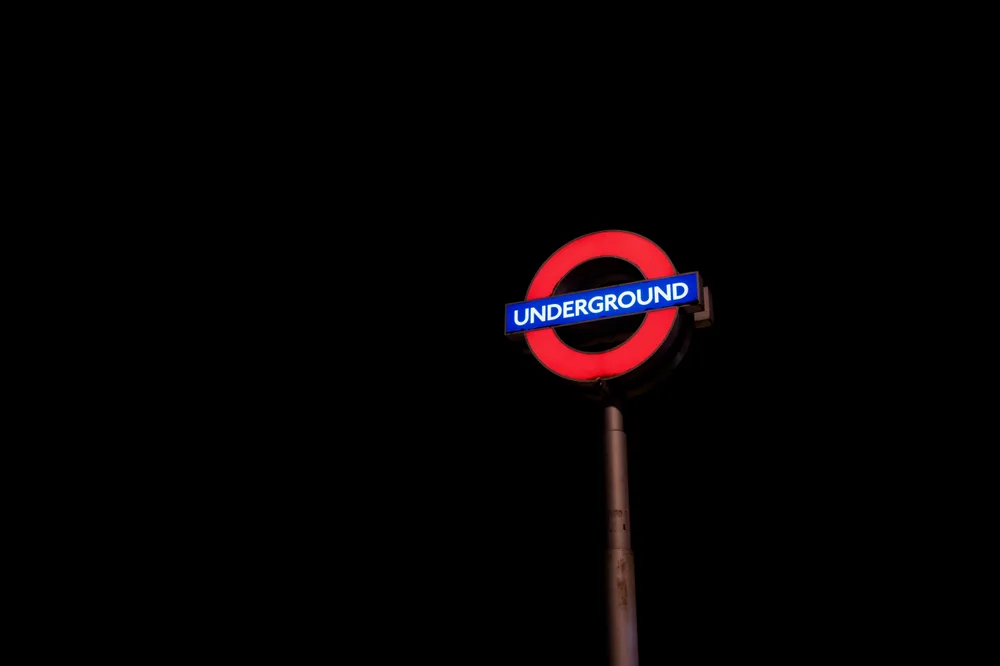 An illuminated red-and-blue London Underground sign against the night sky
