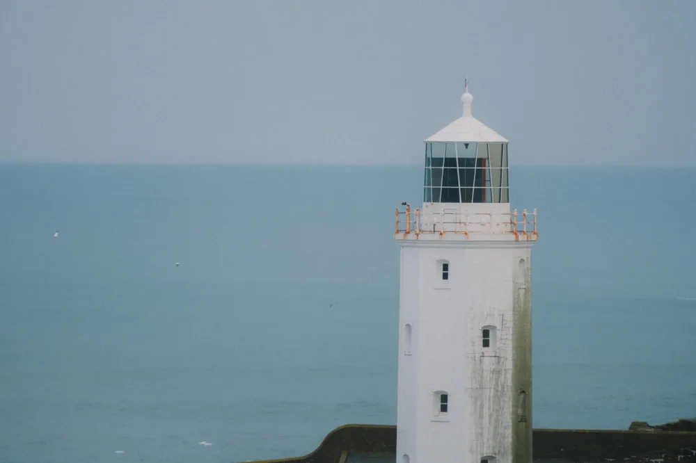 A white lighthouse tower against a calm blue sea